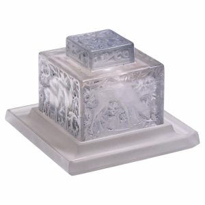 Clear glass decorative cake stand: a square, etched floral box on a matching pedestal atop a white tray with a lid on top.
